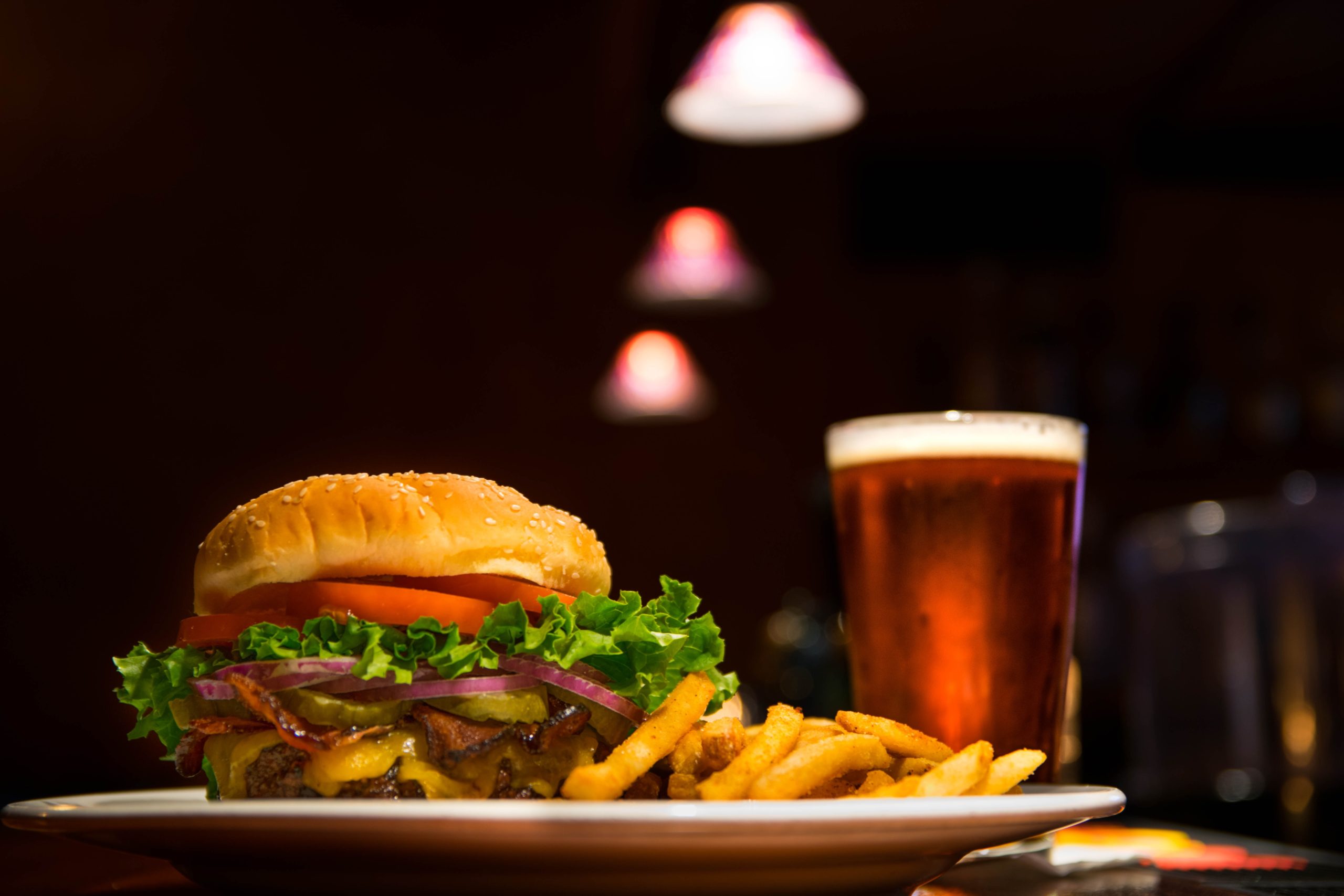 A burger with lettuce, tomato, onion, bacon, cheese, a side of fries and a beer