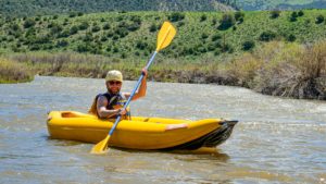 Man on an inflatable kayak on the colorado river with green mountain landscapes behind him
