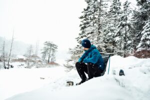 man sitting in winter camping chair in snowy wilderness